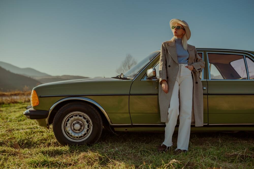 Trendy woman in white wide-leg jeans standing in front of a vintage car 