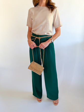 a woman wearing green pants and a gold purse